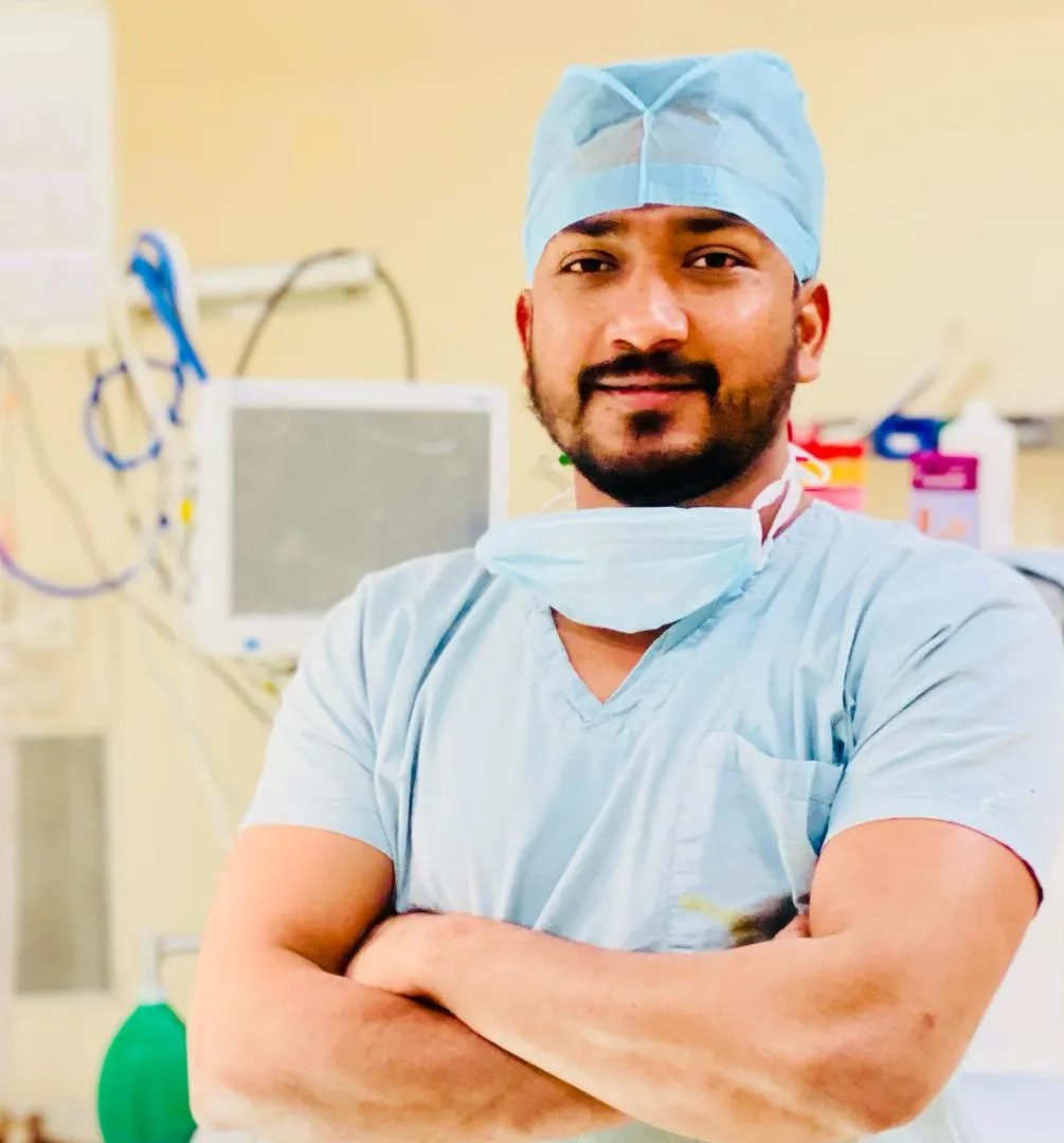 Dr. Nikhil Bansal in surgical scrubs, arms crossed